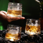 Two spinning crystal whiskey glasses with bourbon held over a dark bar top