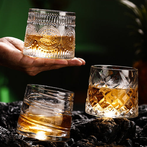 Two spinning crystal whiskey glasses with bourbon held over a dark bar top